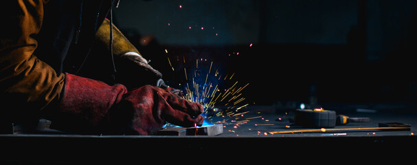 Panoramic shot of craftsman in gloves welding metal profile near working tools on dark background 