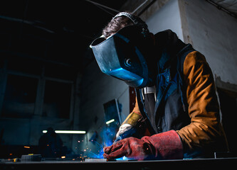 Welder in protective mask with visor and gloves working in factory 