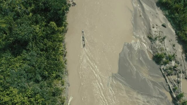 Top view, following a wooden canoe driving over a large river with a brown coloration in a tropical forest
