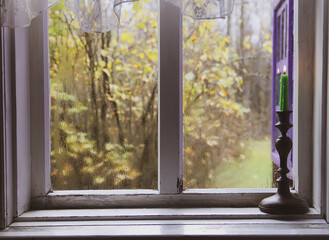 Burning wax candle in brass candlestick on the wooden window sill of in country house interior