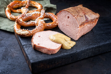 Traditioneller ofenfrischer bayrischer Leberkäse aufgeschnitten und am Stück serviert mit Brezen und scharfen Senf auf einem alten rustikalen Holz Board