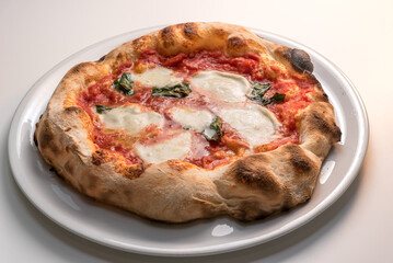 Pizza from Naples, Italy, called margherita because it is dedicated to the queen - pizza with crispy edge, tomato, mozzarella and basil in white plate