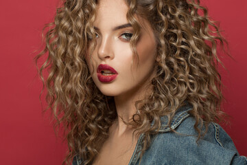 Sensual woman with curly hair on red background, beautiful face close up