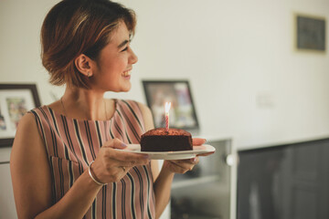 Blurry photo of Woman holding cake with candle while smiling and looking sideways in celebration of...