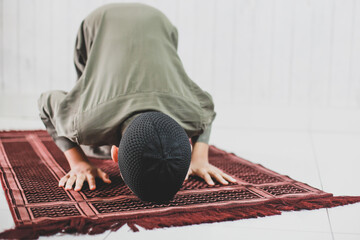 Portrait of asian Muslim Boy wearing traditional costume is doing Salat with prostration pose on...