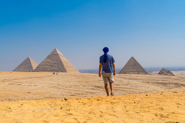 A young man in a blue turban walking next to the Pyramids of Giza, the oldest Funerary monument in...