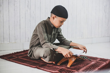 Portrait of asian Muslim Boy wearing traditional costume was reading the holy book Al-Quran on the...