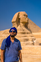 Fototapeta na wymiar Portrait of a young tourist dressed in blue and a blue turban at the Great Sphinx of Giza. Cairo, Egypt