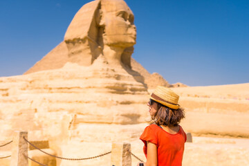 Fototapeta na wymiar A young tourist at the Great Sphinx of Giza dressed in red and with a hat, from where the miramides of Giza. Cairo, Egypt