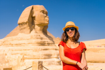 Fototapeta na wymiar Portrait of a young tourist at the Great Sphinx of Giza dressed in red and with a hat, from where the miramides of Giza. Cairo, Egypt
