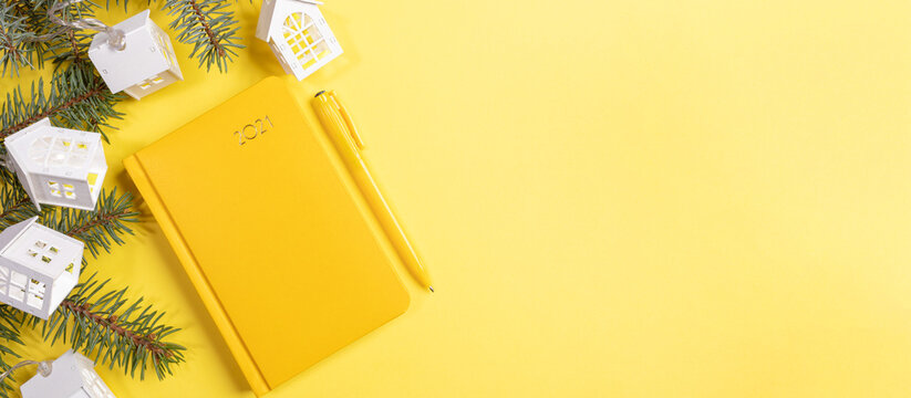 Xmas workspace concept. Yellow background with notepad-organizer on 2021, fir branches and Xmas lights white lodges. Planning for next year. Business greeting card. Top view. Copy space for text.