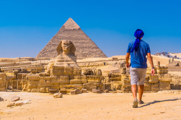 A young man walking towards the Great Sphinx of Giza and in the background the pyramid of Khafre,...