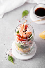 rice noodles with shrimps and vegetables in a glass jar on a white table