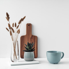 A mug and potted houseplant, a stack of books, a transparent vase and a wooden board. Eco-friendly materials in interior decor, minimalism. Copy space, mock up.