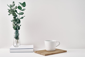 A mug, a stack of books, a wooden board and a transparent vase with eucalyptus branches. Eco-friendly materials in interior decor, minimalism. Copy space, mock up.