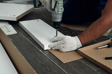Furniture assembly process. Worker in overalls and white footwear. Using a cordless drill, screwdriver. Do it yourself.
