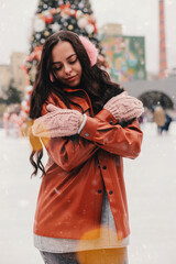 Portrait beautiful happy girl in stylish jacket, warm earmuffs, pink mittens hug herself, skate on...