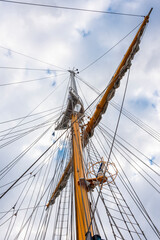View from below on the mast of a large sailing ship against the sky with clouds