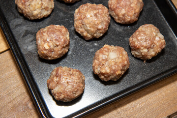 Raw uncoooked beef meat balls on a baking trey ready to be put in the oven