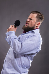 Bearded emotional singer with microphone dressed in shirt studio portrait.