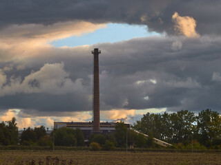 Komin fabryczny i otwarte czyste niebo nad nim, wokół same chmury i smog.