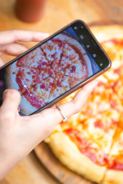 Hand holding phone to take a picture of pizza on the table