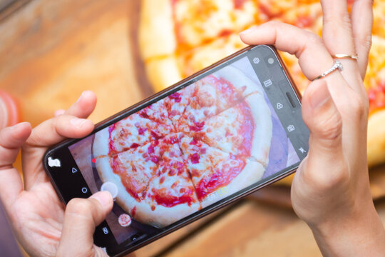 Hand holding phone to take a picture of pizza on the table