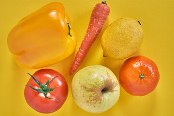 Yellow pepper, lemon, apple, tangerine, tomato and carrot on yellow background. Healthy vegetarian food.