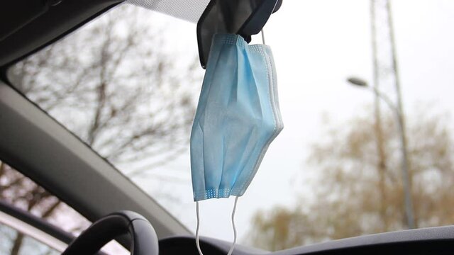 Blue hygienic mask hanging on a car interior mirror