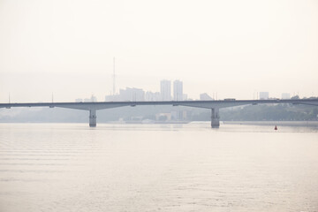 Fototapeta na wymiar road bridge over a wide river and the silhouette of a distant city behind it in the morning fog