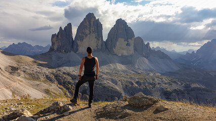 Fototapeta premium A man in hiking outfit standing on top of Sextner Stein and enjoying the view on the famous Tre Cime di Lavaredo (Drei Zinnen), mountains in Italian Dolomites. Desolated and raw landscape. Freedom