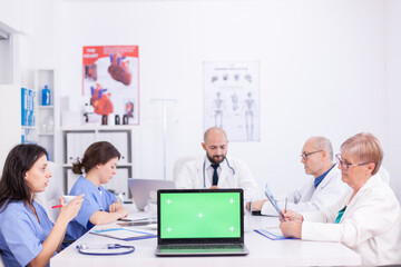 Laptop monitor with green screen in hospital conference. Clinic expert therapist talking with colleagues about disease, medicine professional.