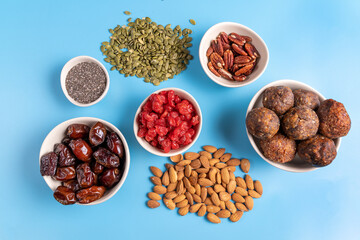 Collection of Superfoods and nuts in Bowls for health, fitness and vitality used for preparing energy balls. Top view. On blue background.