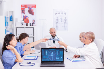 Matude doctor giving radiography to young nurse during staff meeting in conference room. Clinic expert therapist talking with colleagues about disease, medicine professional.