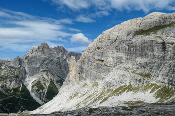 Fototapeta premium A panoramic view on Dolomites in Italy. There are sharp and steep mountain slopes around. Lots of lose stones and pebbles. The sky is full of soft clouds. Raw landscape. Serenity and calmness