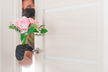 Man in mask gives bouquet of flowers through the doorway