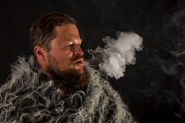 Fototapeta na wymiar Solid bearded man dressed in a fur mantle exhaling vapour