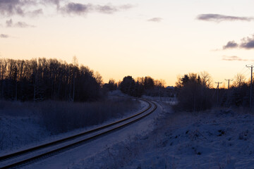A beautiful winter morning landscape of a railway tracks in the forest. Colorful sunrise scenery of Northern Europe.