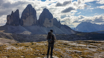 A man in hiking outfit enjoying the view on the famous Tre Cime di Lavaredo (Drei Zinnen), mountains in Italian Dolomites. Desolated and raw landscape, full of lose stones. Overcast. Achievement