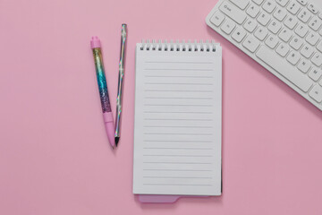 Flat lay of weekly planner, clear notepad, keyboard, glitter holographic pens are on pink background. Concept of online, homeschooling, back to school, home office. Blank, copy space.