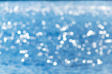 Delicate blue texture bokeh sea. Summer background. Blurry blue bokeh glare on the water on a sunny...
