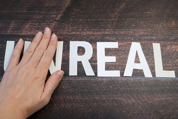 hand changes the word unreal to real on wooden background, closeup