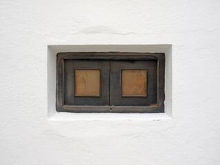 Obraz na płótnie Canvas Small vintage wooden window with grate in white lime wall. Old window on white cement wall. Architecture and construction detail. Masonry pattern.