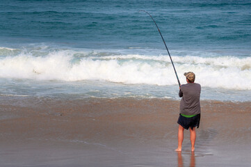 One solitary man bait fishing in the Indian Ocean on a warm winter day when the sun is setting. Cape Vidal beach, KwaZulu-Natal - South Africa 