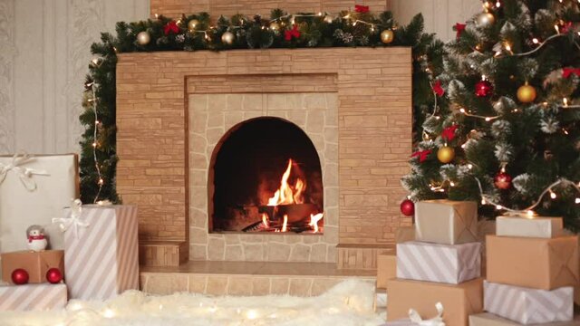 Footage of heap of gifts next to burning fireplace and glowing Christmas tree in living room on Christmas eve, cosy festive room, New Year celebration.