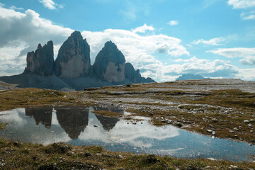 A panoramic view on the famous Tre Cime di Lavaredo (Drei Zinnen), mountains in Italian Dolomites. The mountains are reflecting in small paddle. Desolated and raw landscape. Natural phenomenon
