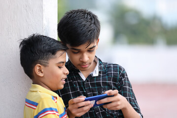 Indian little brothers playing mobile game at home terrace