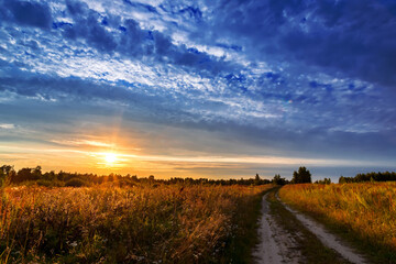 Road to the field and sky with clouds on sunset. Summer landscape.