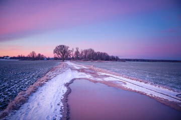 A beautiful winter morning landscape with a gravel road. Bright, extra colorful scenery of Northern Europe. Snow covered road in the rural scene.