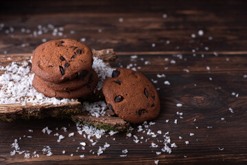 Four chocolate chip cookies on a dark wooden background with snow